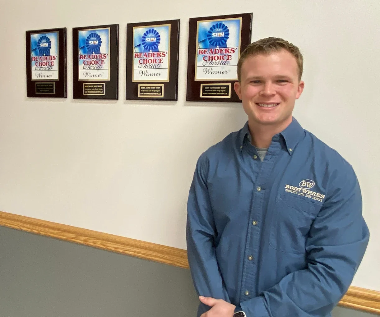 Karl Linton, owner of Bodywerks Auto Body Repair, standing in front of the shop's five Readers' Choice award plaques